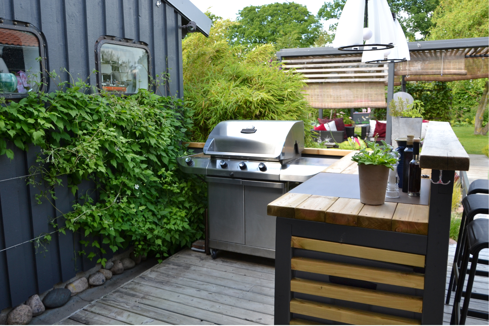 Utekjøkken med grill og barløsning på terrasse i hagen Terrasse med gassgrill, barløsning og grønne planter ved mørk husvegg.